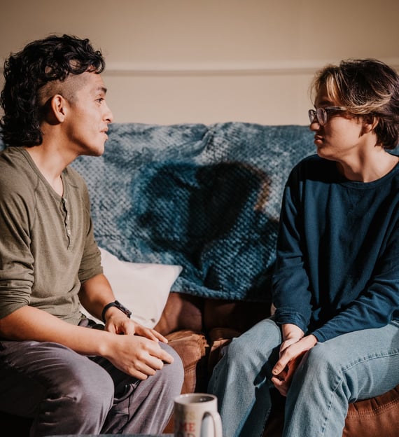two actors sitting on a couch portraying best friends in anew original play by Trent Clifford.