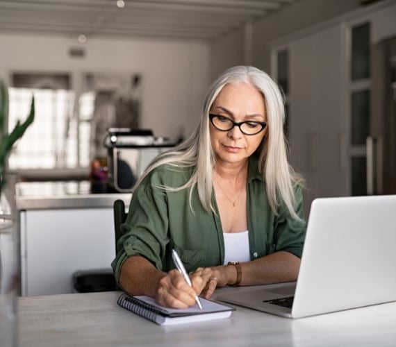 a woman in glasses and a green shirt is sitting at a desk with a notebook