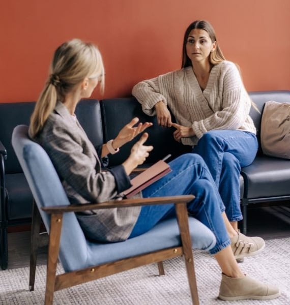 a woman sitting on a couch talking to another woman