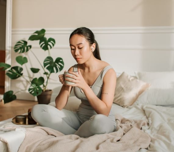 a woman sitting on a bed with a cup of coffee