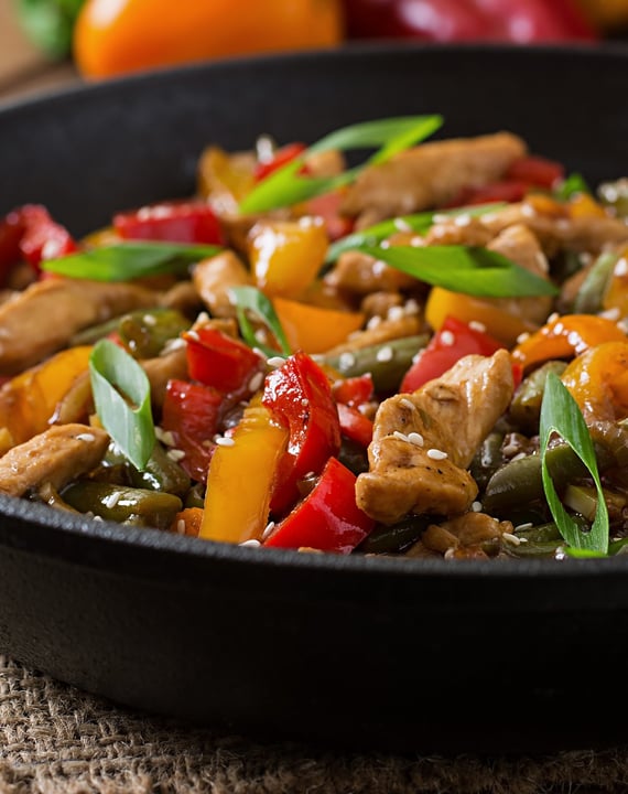 Prato de frango xadrez com pimentões, cenoura, cebola e ervilhas, decorado com cebolinha e sementes 