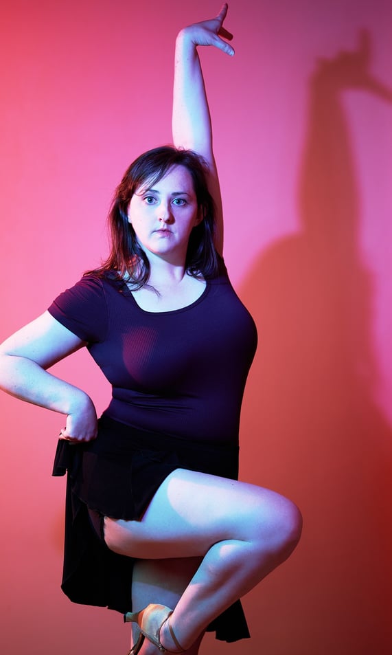 a woman in a black dress and heels is posing as a dancer in front of pink background
