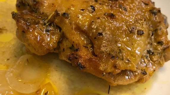 Juicy baked chicken thigh on a white plate with broth and onions