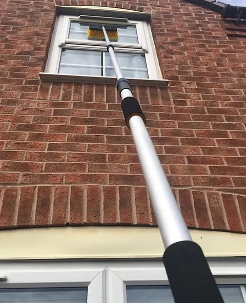 brush on an extension pole cleaning a window on a house in droitwich