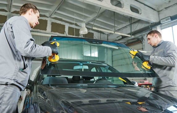 two workers lift a windshield into place