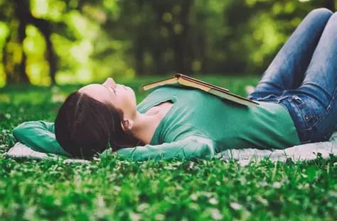 Femme allongée dans l'herbe, jambes repliées, pieds sur le sol et un livre ouvert sur sa poitrine