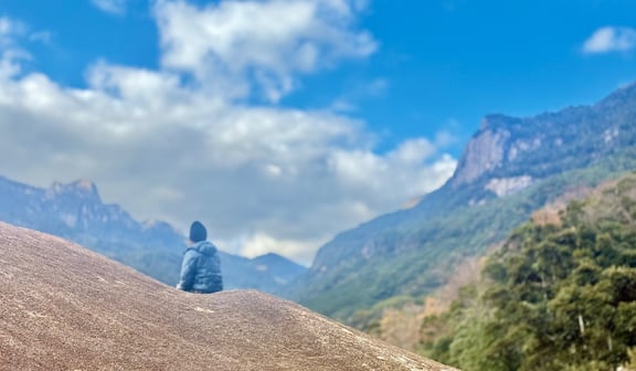 raveler sitting on a mountaintop gazing toward distant volcanic peaks beneath a blue sky in Japan