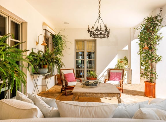 Terrace with wooden seating, pink cushions, plants, and a chandelier in rustic style.