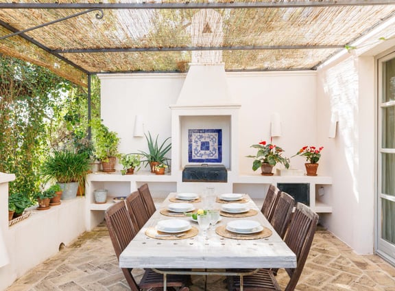 Outdoor dining with wood table, tiled grill, fireplace, vines, and potted plants.