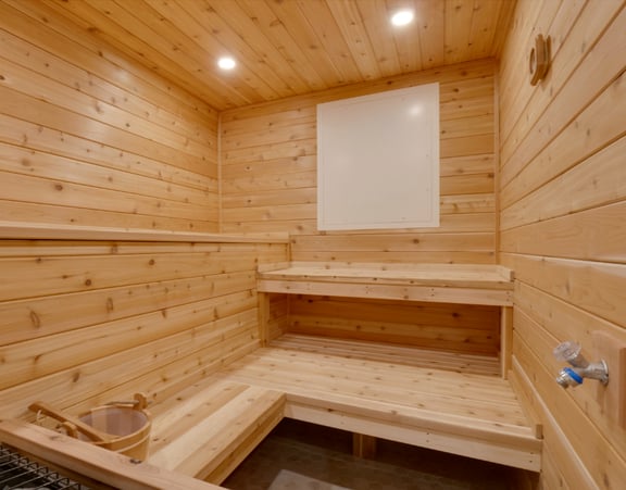 A wooden sauna with a wooden bench and a bucket of water