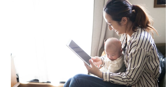 Madre sentada  con un bebe de pocos meses en brazos viendo una tablet