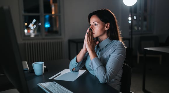 Mulher sentada na frente do computador com as mão juntas a frente do rosto preocupada