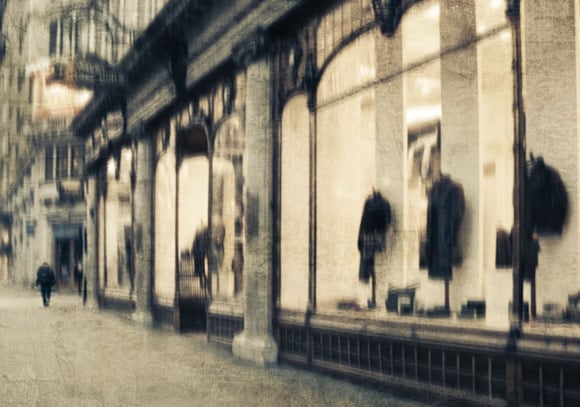 Softly blurred London street scene with a pedestrian walking past illuminated shop windows displaying coats and reflections