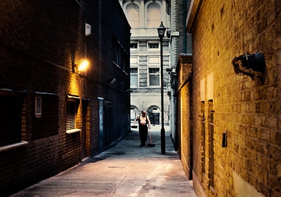 An early morning photograph of an elderly man without a shirt cleaning an alleyway in central London, captured early morning