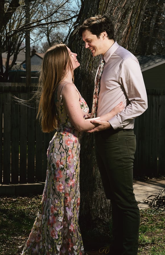 a man and woman facing each other and standing in front of a tree