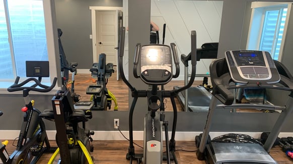 home gym/exercise room with a spin bike, rower, elliptical and treadmill in front of a large mirror