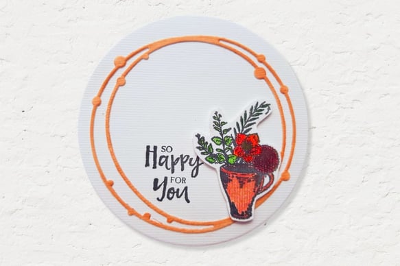 A round card with an orange circle border features a painted orange mug filled with green leaves and