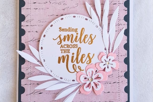Greeting card with the message "Sending smiles across the miles" in gold on a round white cutout. Pi