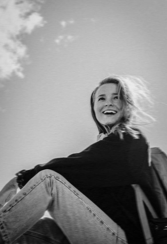 black and white photo of a young explorer woman sitting outdoors and smiling