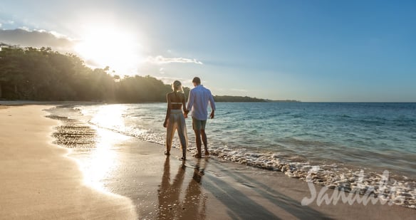 Coastal Vibe Travel - Sandals Honeymoons - a couple holding hands and walking on the beach