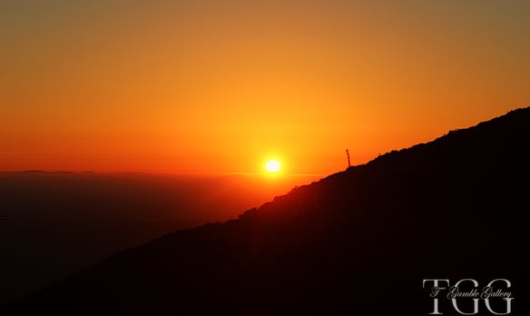 a sunset on a hill with a cross on the top of a hill