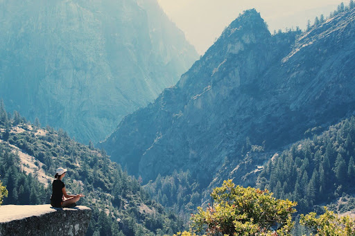 Woman meditating to relieve her mental health atop of a cliff within a mountain of forest