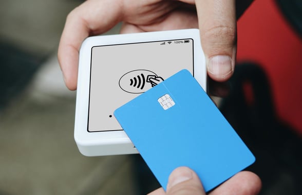 Person making a contactless payment with a blue card on a mobile payment terminal.