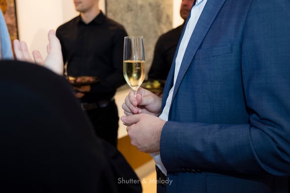 Mann in blauer Jacke mit einem Glas Sekt in der Hand.