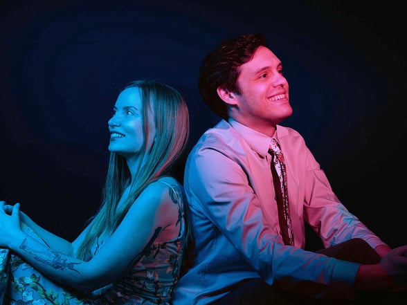 a man in red light and woman in blue light sitting back to back looking at opposite direction