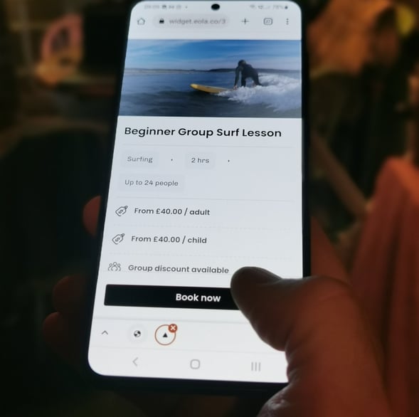 A mobile phone displaying a beginner group lesson booking page, a thumb about to click book now