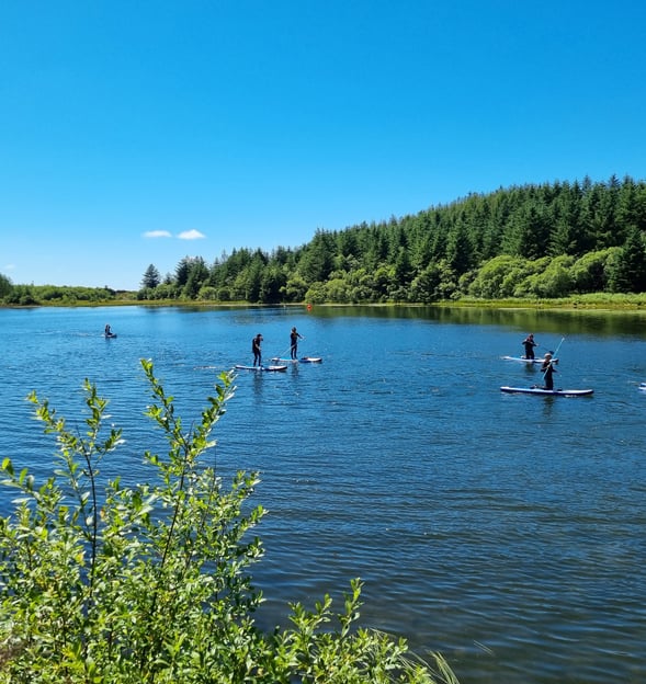 A calm lake with sunshine and blue skies as a stand up paddle board group practice standing