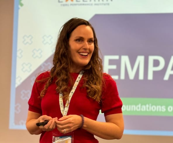 a woman in a red shirt and black pants speaking in front of a screen saying Empathy