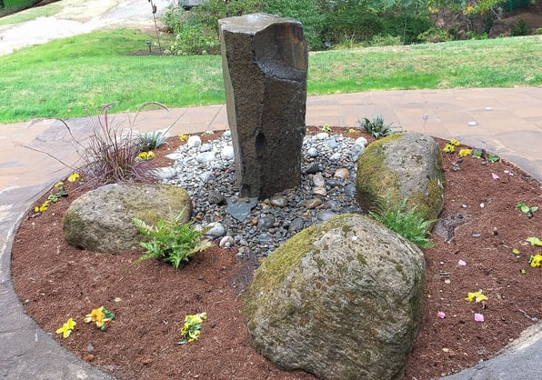 Columnar granite waterfall bubbler surrounded by river rock and large decorative boulders