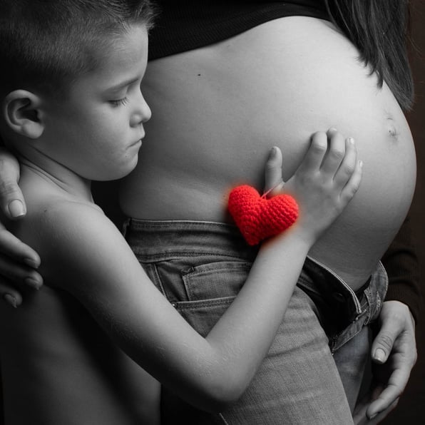 niño en blanco y negro con corazon en rojo, toca la tripa de su mama .