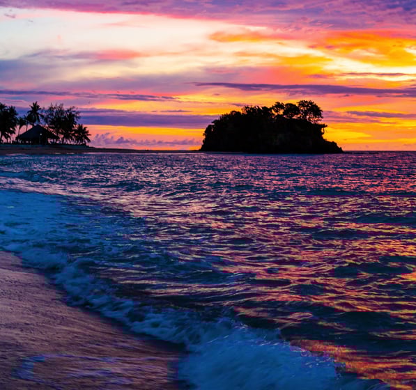 a sunset on a beach with a small island in the background