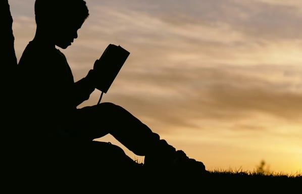 Silhouette of a person reading a book at sunset