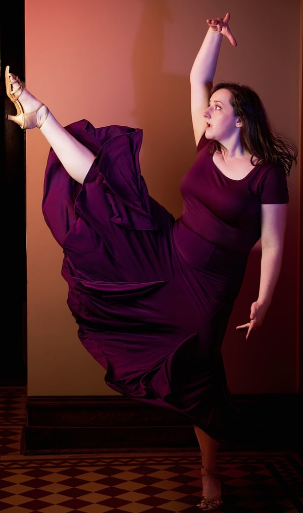 a woman in a purple dress with one leg up dancing in a latin dance style
