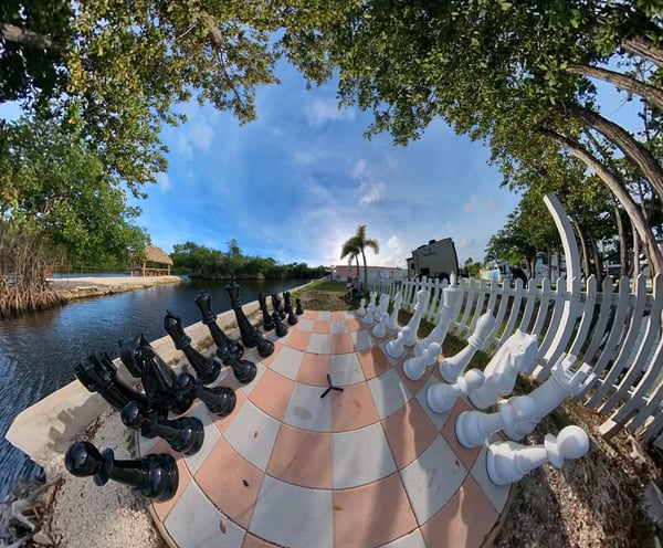 a chess game with chess pieces on a checkered floor next to the waterfront