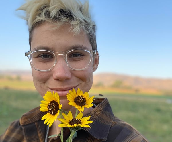 Audio engineer Hannah Copeland holds yellow flowers in front of her face and smiles outdoors.