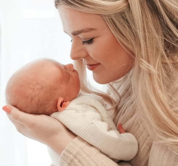 Newborn baby sleeping in mother’s arms, neutral tones, natural light