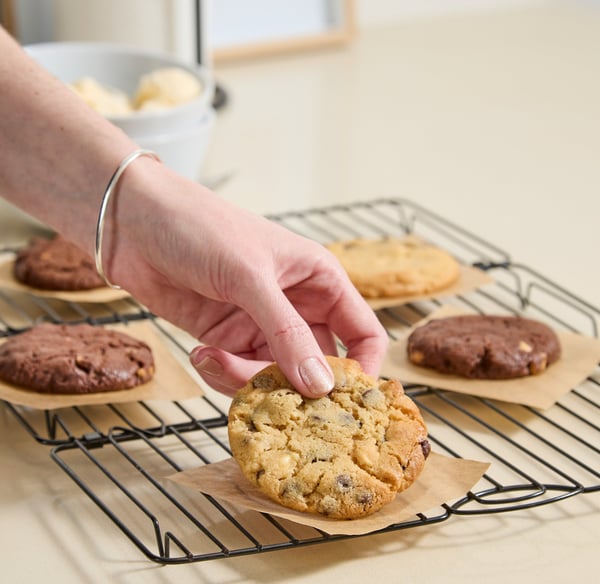 A hand picks up a freshly baked vanilla choc chip cookie.