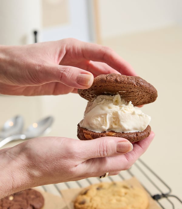 Two chocolate Quickie Cookies being placed together around a scoop of ice cream. 