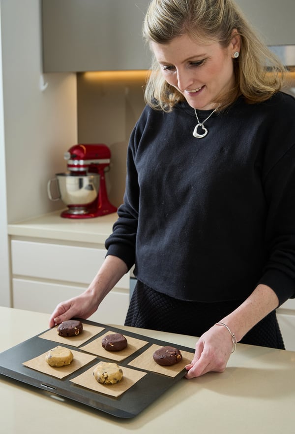 Olivia, Chief Cookie Officer, smiles down at a tray of frozen cookie dough pucks ready for the oven.