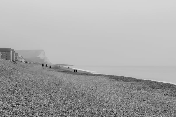 A black & white photo along seaford beach where people are walking along towards the cliffs in the distance