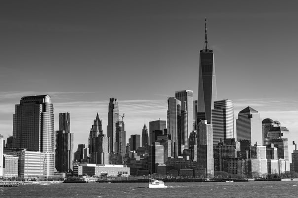 A black and white photo of New York City skyline taken from the Hudson River. in the forground is a pleasure boat passing