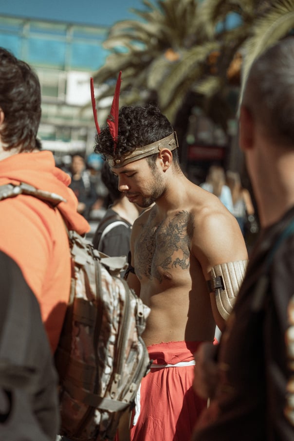 Shirtless person with a decorative headpiece and tattoos at Japan Weekend Bilbao. Surrounded by a crowd. Cosplay event atmosp