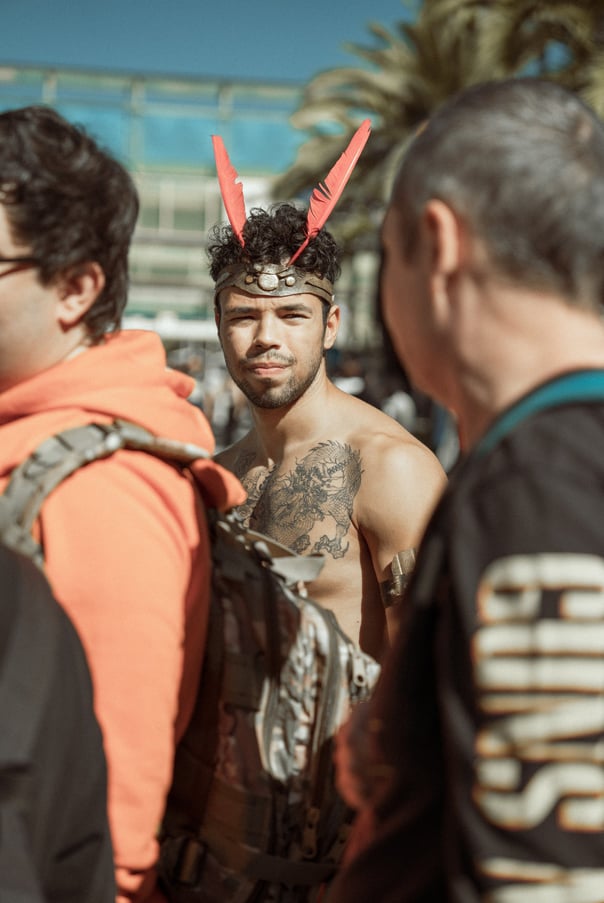 Man with tattoos and red feather headpiece at IFEMA Madrid. Unique convention costume