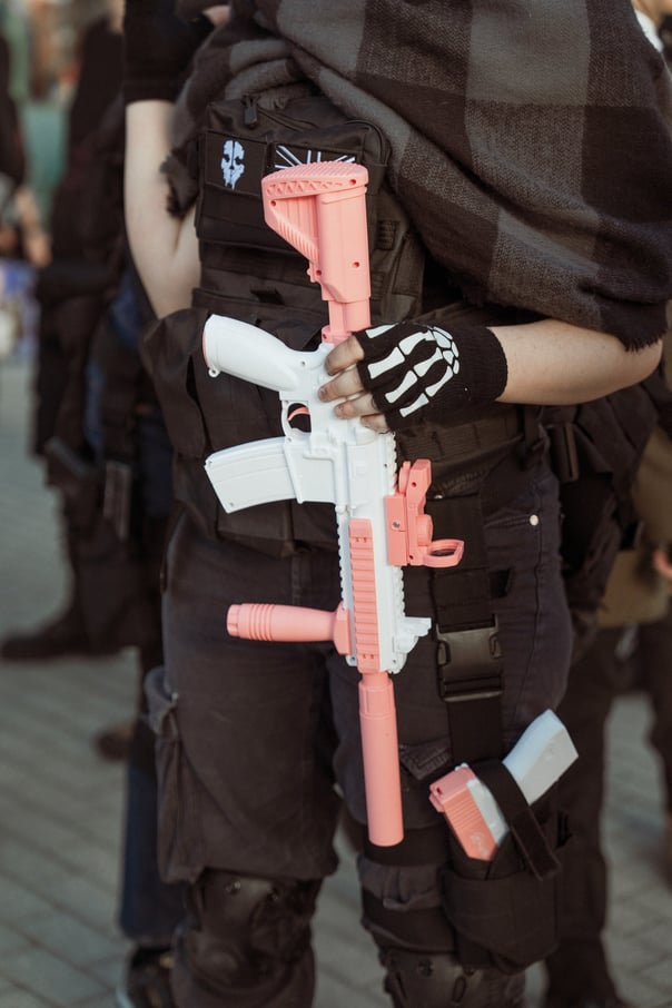Cosplayer in dark tactical clothing with a pink and white toy rifle at IFEMA Madrid. Convention prop
