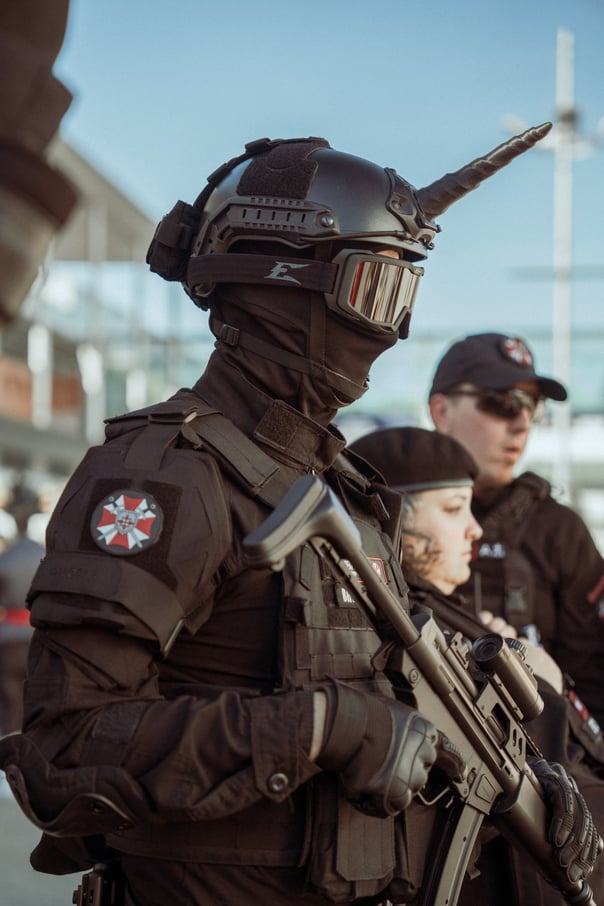 Group of cosplayers in black tactical gear with Umbrella Corporation patches and prop weapons at IFEMA Madrid. Resident Evil 