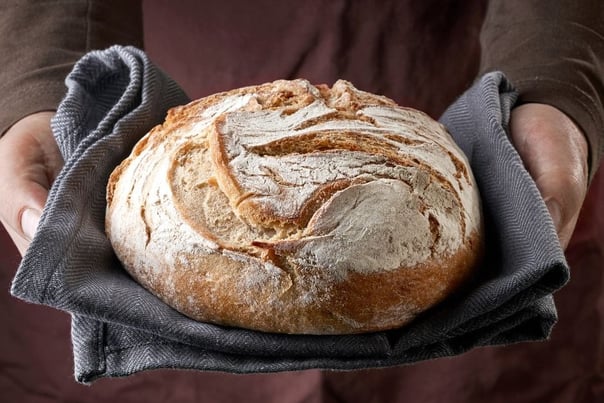 a person holding a loafed breaded bread in a kitchen